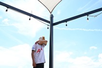 A man wipes his forehead under the hot sun as he walks under shade sail.