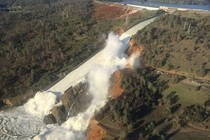 Water pours over the damaged main spillway at the Oroville Dam and over a hillside.