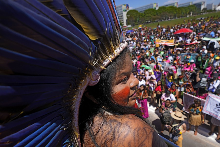 A person wearing a feathered headdress speaks to a crowd of people.