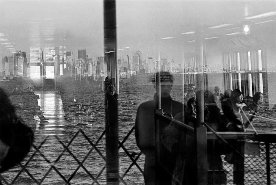 Photo of reflection in window looking out from Staten Island Ferry at skyline, where two sunlit doors almost reflect as phantom mirage of Twin Towers