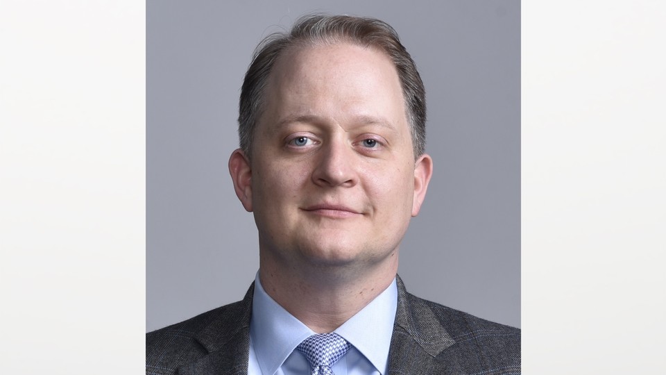 A color headshot of Shane Harris wearing a gray suit and blue shirt and tie