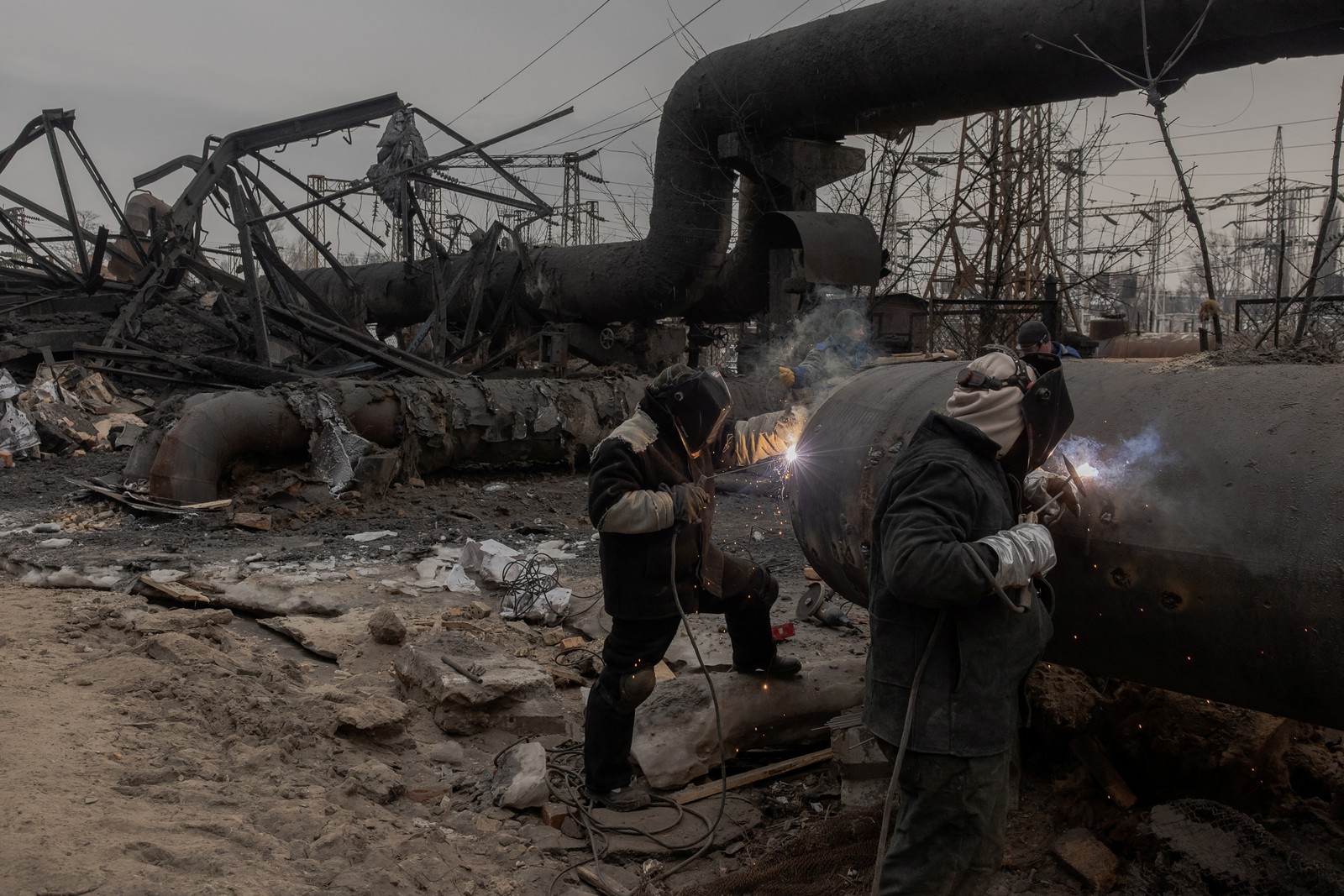 Workers with welding gear work on damaged equipment in a yard littered with debris from a missile attack.