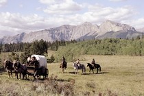 people ride in a covered wagon with mountains in the background
