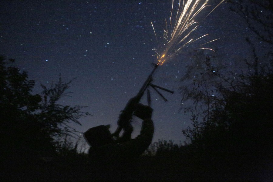 A soldier fires his weapon at the night sky.