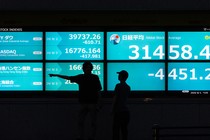 A photo of two people silhouetted against a digital display that shows falling stock indexes