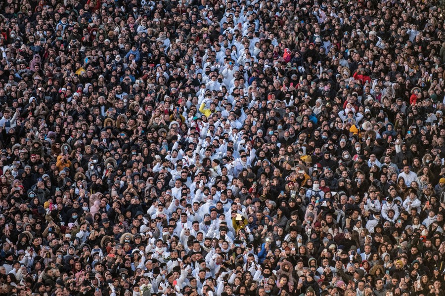 A large crowd of people watch as a religious procession begins.