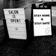 A photo of two road-side signs. One says, "Salon is open!" The other says, "Stay home and stay safe!"