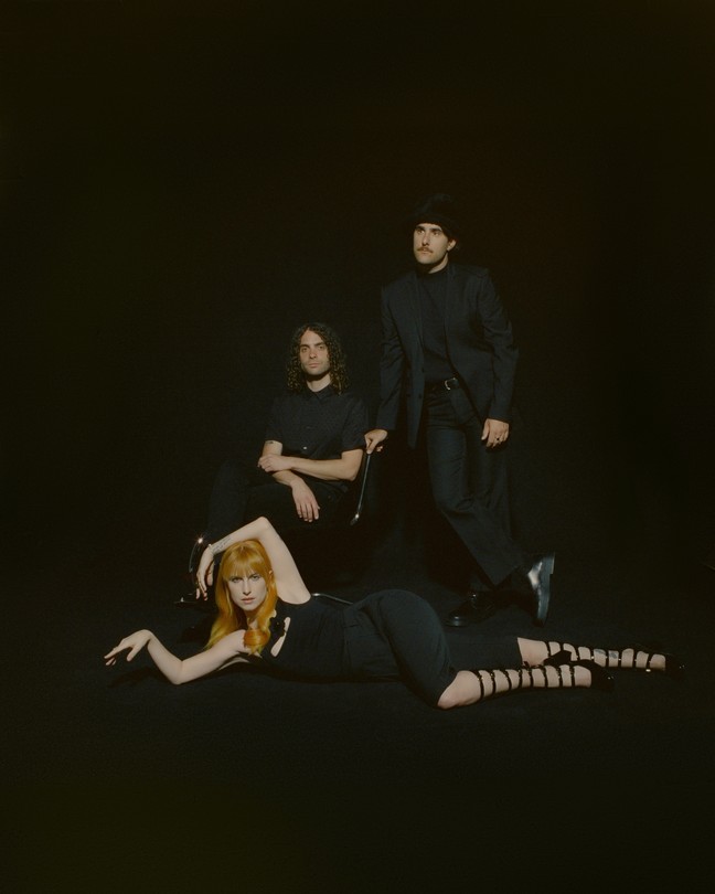 The three members of Paramore dressed in black against a black background