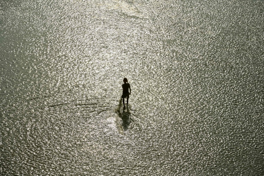 A person with a fishing net walks in a shallow section of a river.