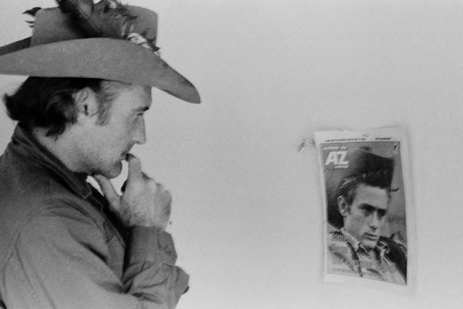 Man in cowboy hat looking at magazine cover hanging on a wall