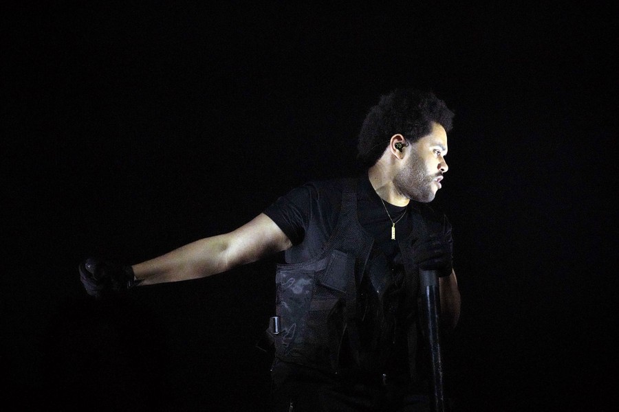 A view of the performer known as The Weeknd, lit up on a dark stage.