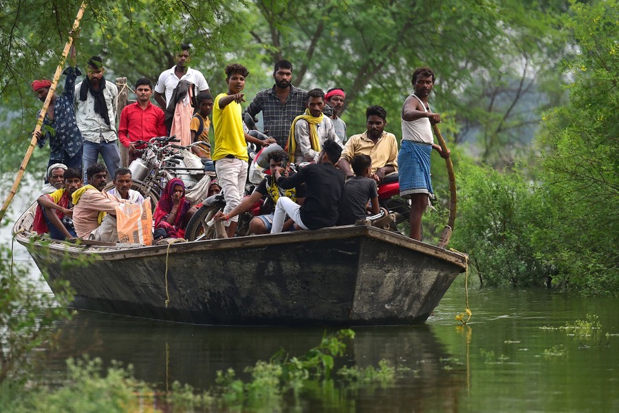 About two dozen people crowd onto a boat moving through calm floodwater.