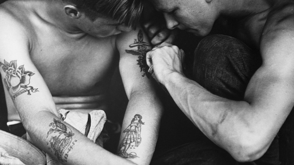 a black-and-white photo of someone getting their upper arm tattooed