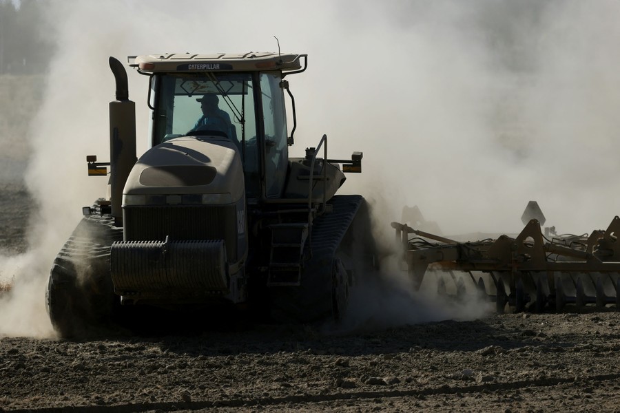 A tractor kicks up dust as it plows a dry field.
