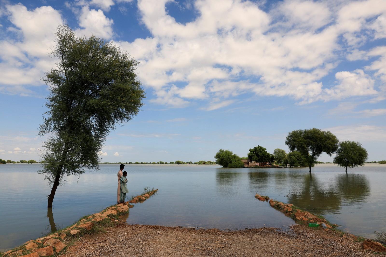 Two boys stand near a partially-submerged road during a flood.