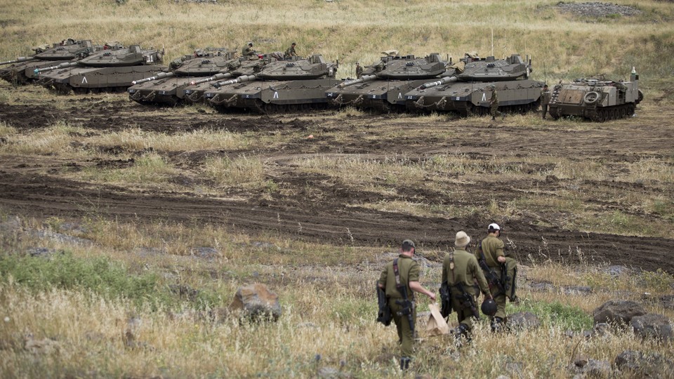 Three soldiers walking in front of a line of tanks