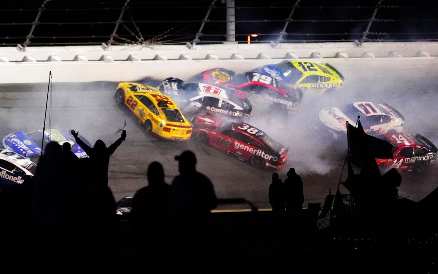Many race cars crash on a sloped race track.
