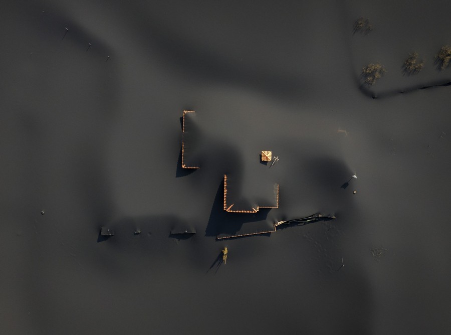 Smooth drifts of dark gray ash cover a landscape and house, seen from above.