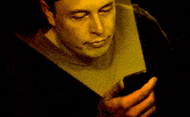 Elon Musk looking at a smartphone whose screen lights up his face in pulsating glow