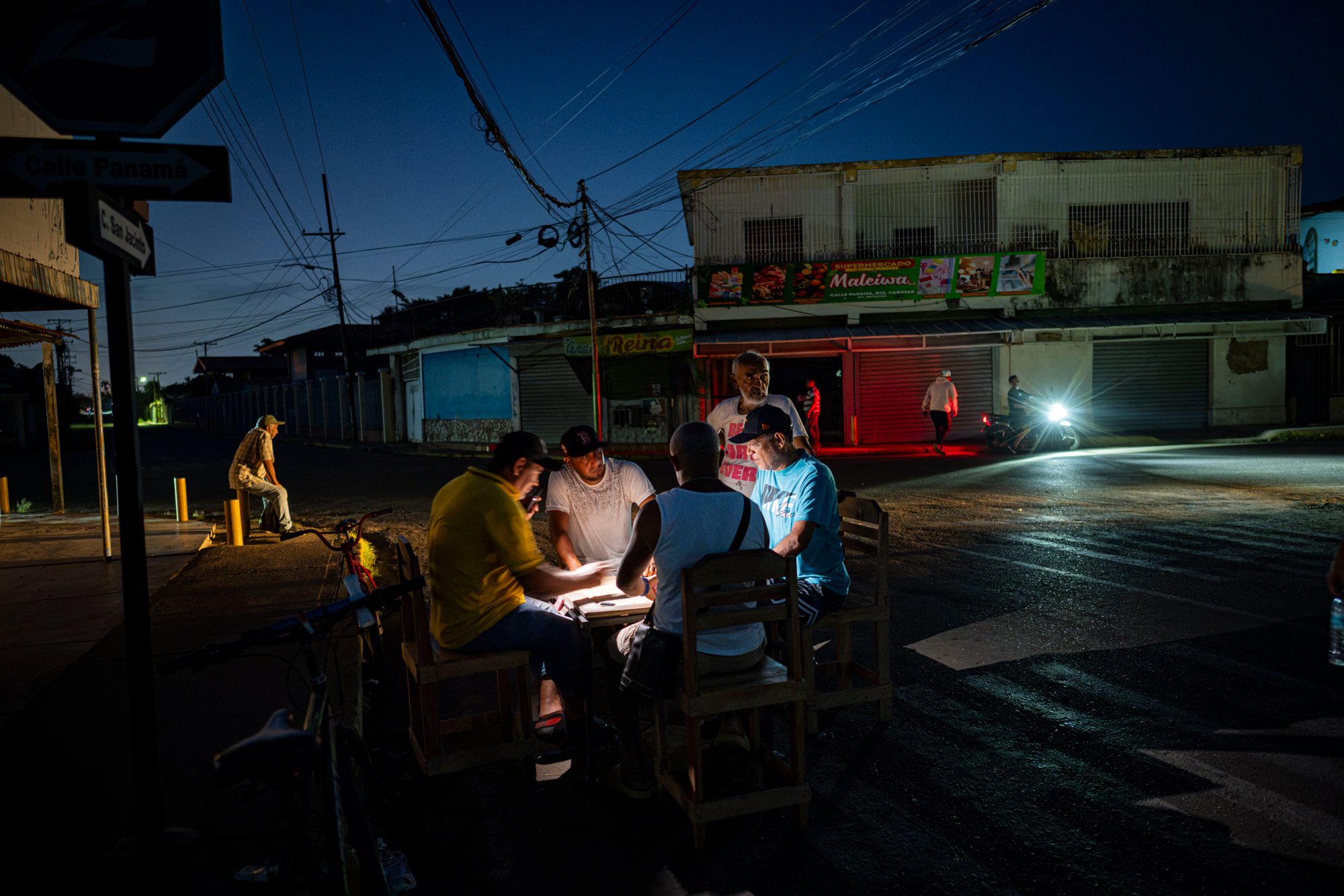 four men play checkers at night while a fifth watches at a table set up in the street
