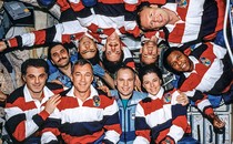 group photo of 10 astronauts in space station, some upside down, most wearing matching red, white, and blue polo shirts