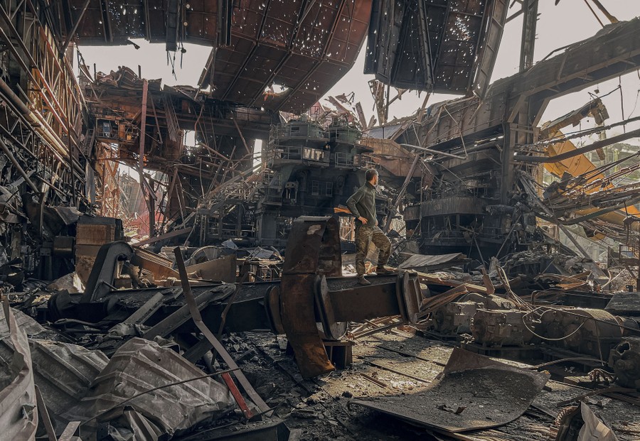 A soldier is completely surrounded by wreckage and ruin, the bomb-destroyed remains of a huge factory all around.