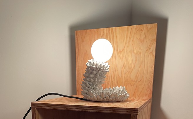 A lamp made out of clay spikes, sitting on a wooden chair.