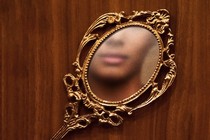 a fancy mirror on a wooden surface, the face of a black woman is reflected in the mirror