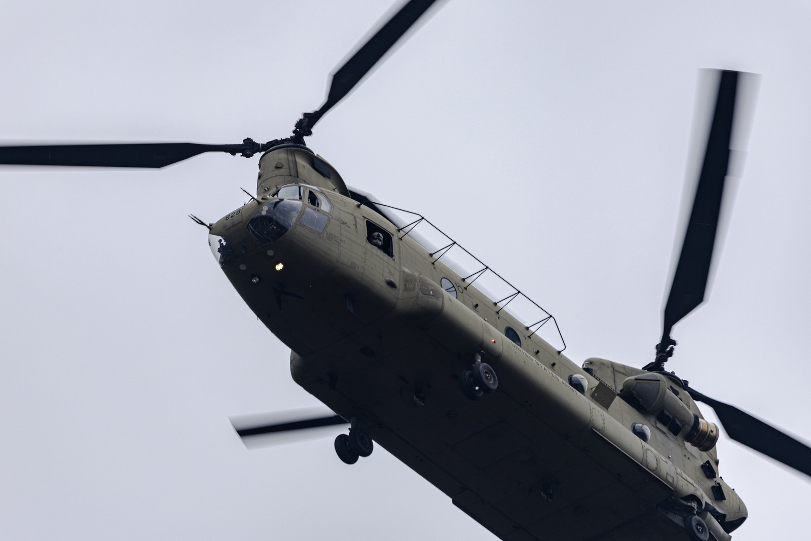 A twin-rotor military helicopter flies close overhead.