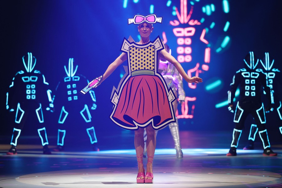 A model poses onstage, wearing a life-size cutout-doll dress.