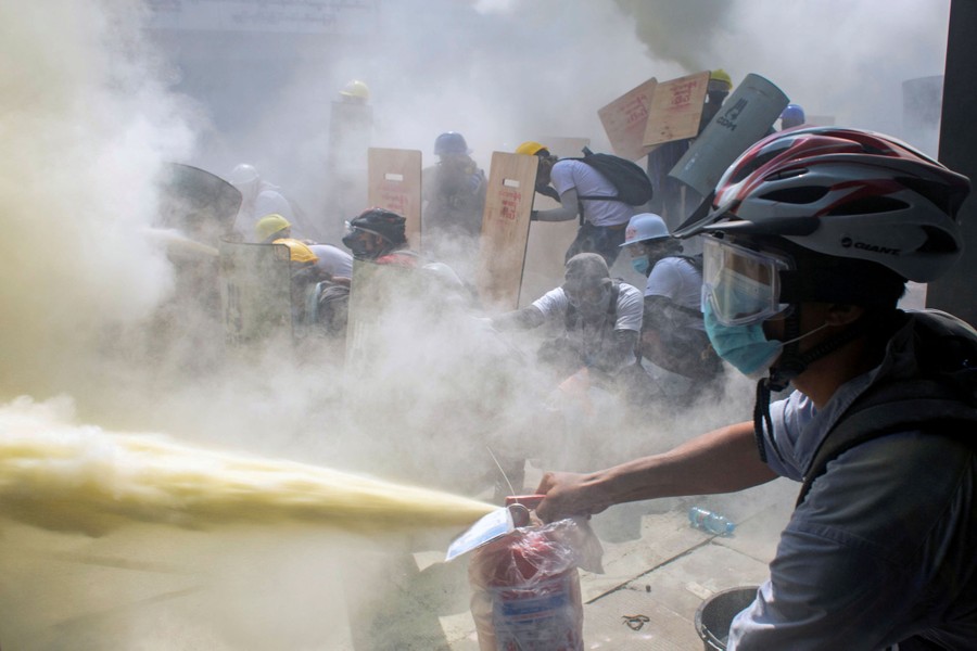 A protester sprays a fire extinguisher as demonstrators clash with riot police in a street.