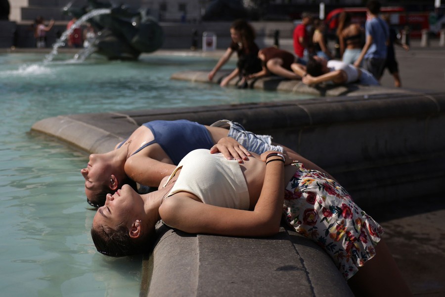 Two women lay back to dip their hair into the water of a fountain.