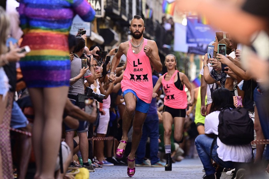 Several runners compete in a race while wearing high heels, surrounded by cheering onlookers.