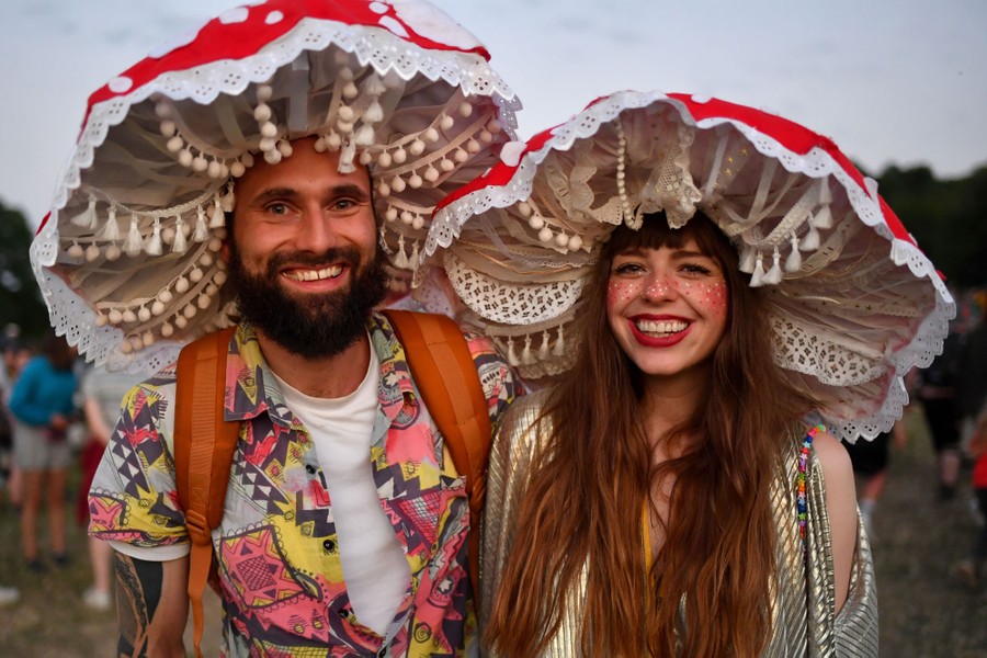 Two people wear large, ornate hats resembling mushroom tops.