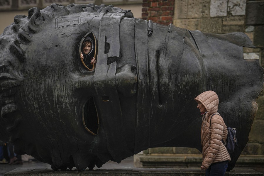 A child looks out from the open eye of a large, hollow sculpture of a head.