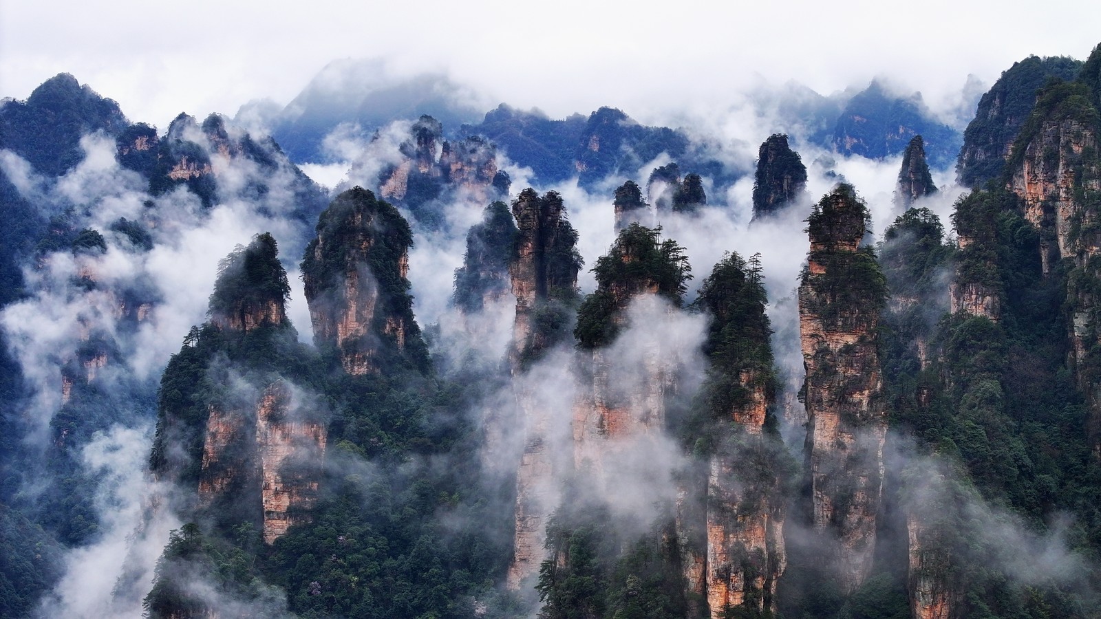 Tall stone formations, topped with trees, shrouded by low clouds