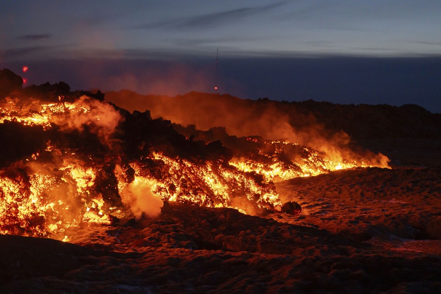 Molten lava flows across a plain, seen at night.