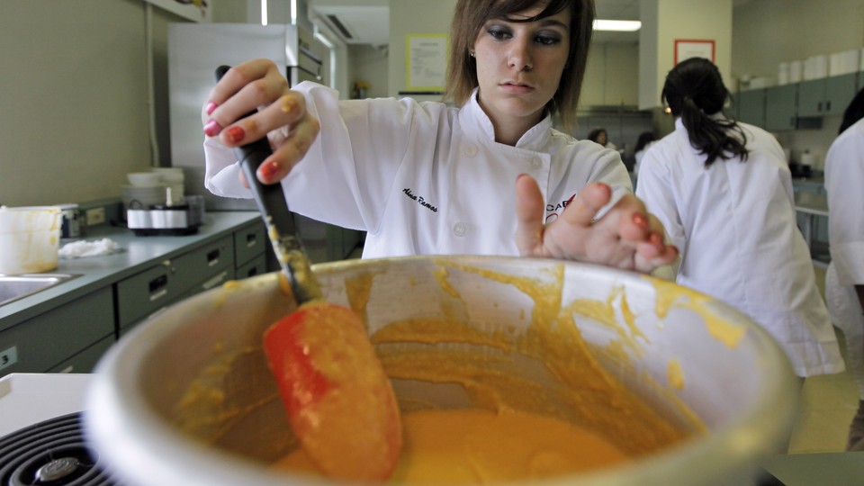 A woman in a chef's uniform stirs a pot containing an orange paste.