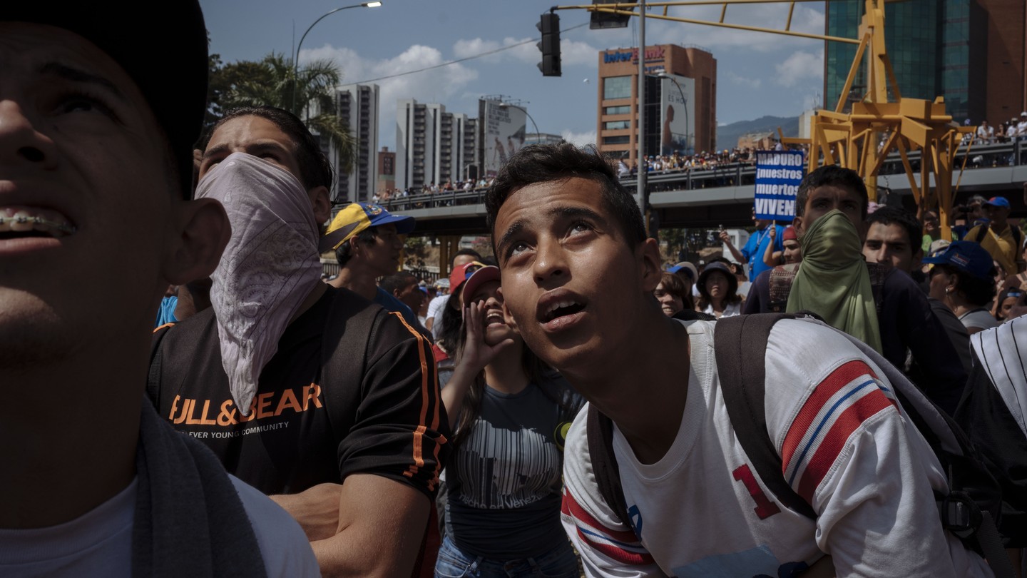 Protesters look at a flag of Maduro burning near Las Mercedes in Caracas.