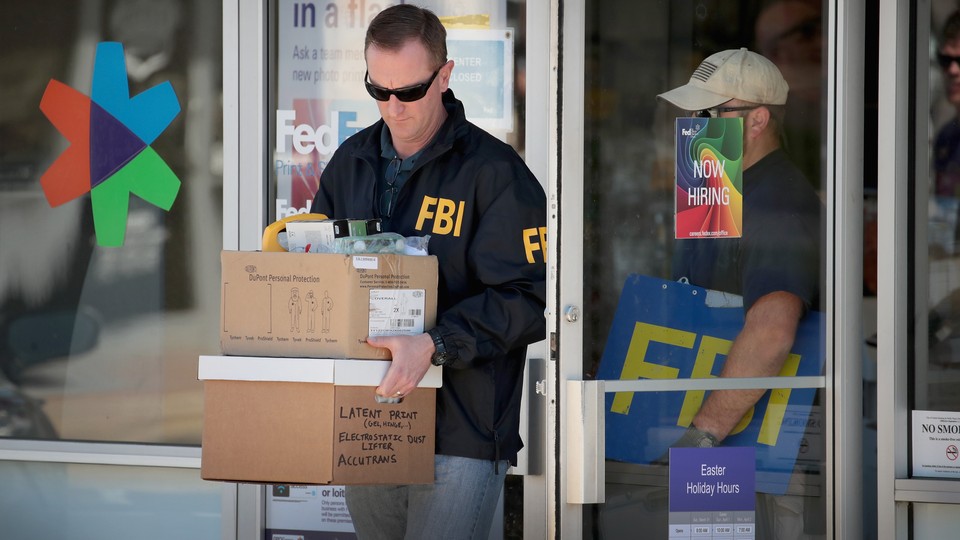 A man in an FBI jacket carries boxes out of a FedEx center.