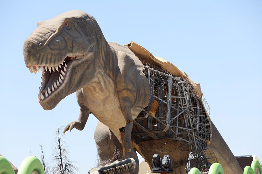 A life-size statue of a T-Rex with much of its fiberglass skin fallen away, exposing the underlying metal support structure