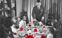 A black-and-white photo of a family sitting down for a holiday dinner, overlaid with red coronavirus particles