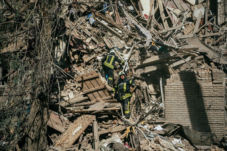 Ukrainian firefighters stand on the rubble of a building after a missile strike.