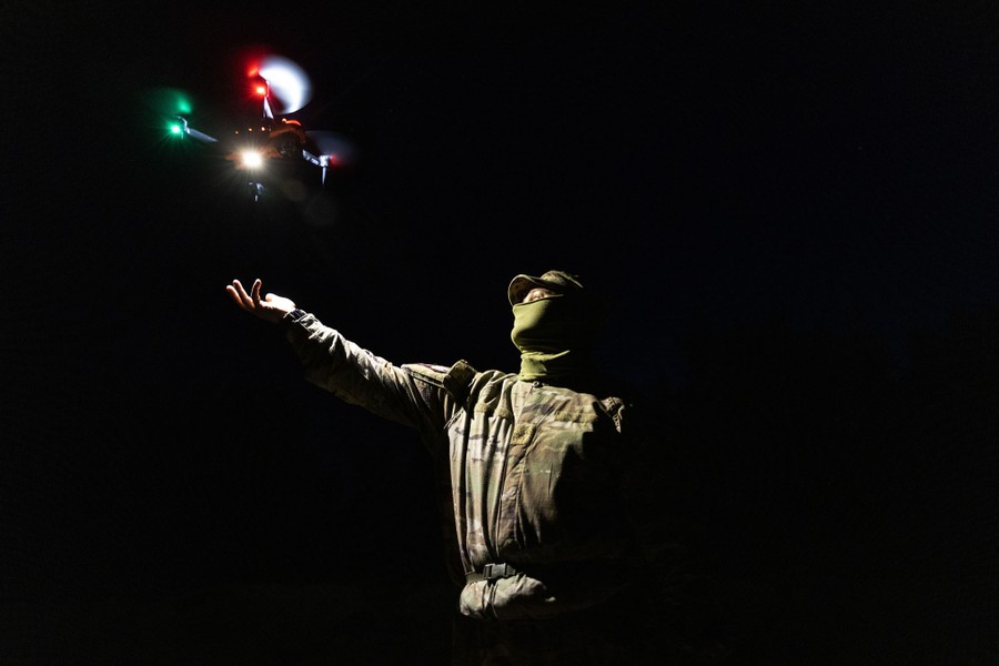A soldier stretches out their hand to launch a small drone at night.