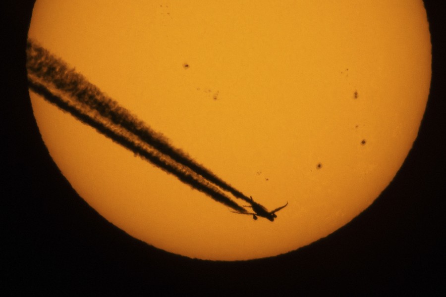 An aircraft and its contrail, silhouetted against the sun