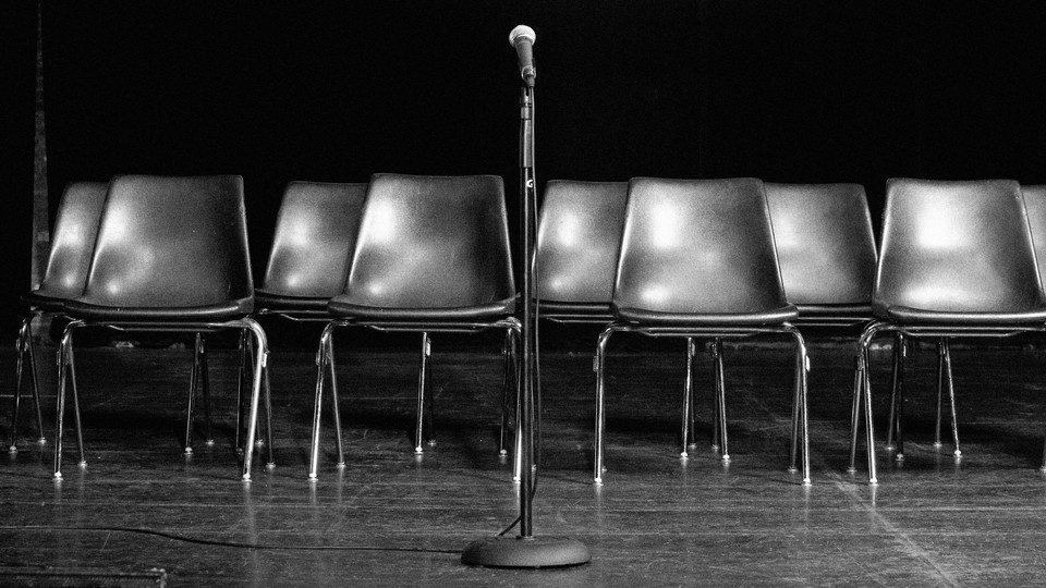 Empty chairs are pictured on a stage behind a standing microphone.