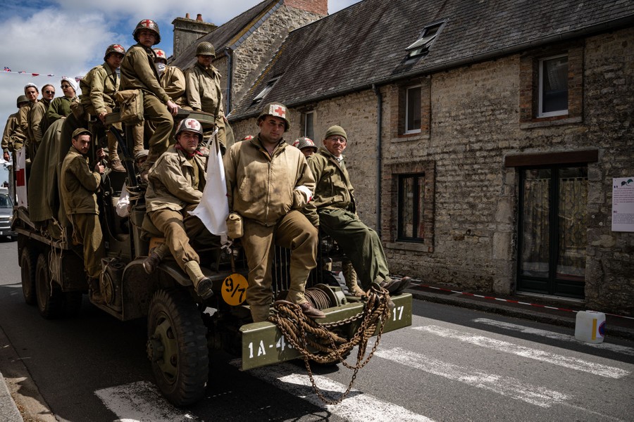 People wearing replica WWII military attire ride atop a WWII-era military truck in a French village.
