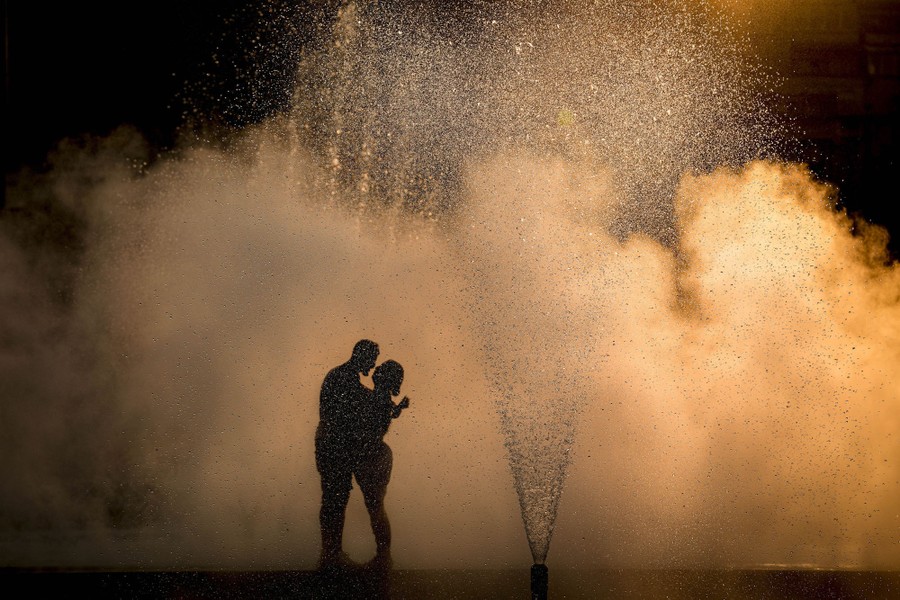A couple hugs near a fountain at sunset.