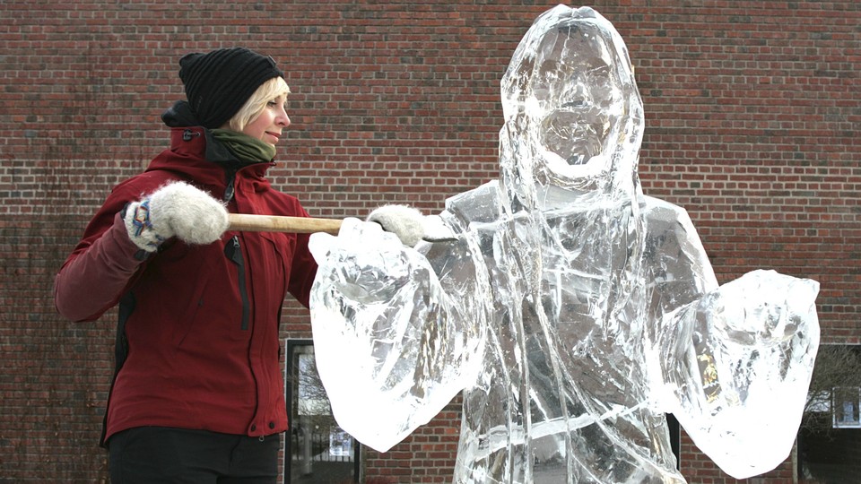 A woman raises an ice-scraping tool next to an ice sculpture of Jesus Christ.