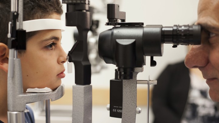 A young boy has his eyes examined by a doctor